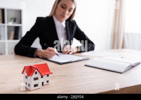 fuoco selettivo del modello della casa e contratto di firma del notaio sfocato su sfondo sfocato Foto Stock
