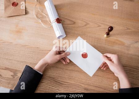 vista dall'alto del notaio tagliato che tiene la busta sigillata vicino allo stampo e al contratto laminato Foto Stock