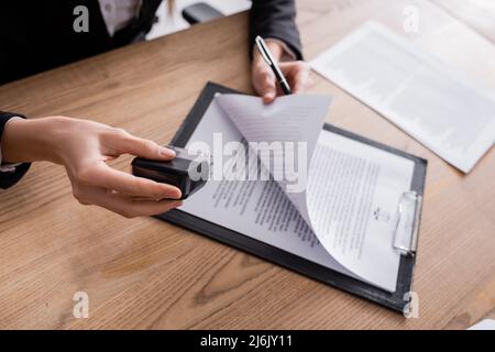 vista ritagliata dell'avvocato che tiene stampatore e penna vicino al contratto sulla clipboard Foto Stock