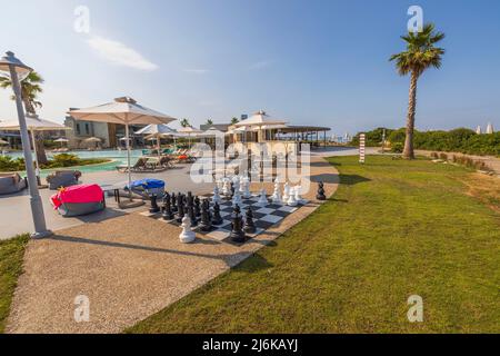 Vista dei giardini dell'hotel con grande scacchiera e enormi pezzi di scacchi bianchi e neri per giocare all'aperto. Grecia. Foto Stock