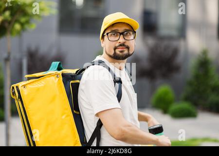 Ritratto di un giovane uomo portacolonata che guida scooter elettrico con zaino termico giallo. Corriere che consegna cibo o pacchi. Concetto di servizio di consegna rapida. Foto Stock