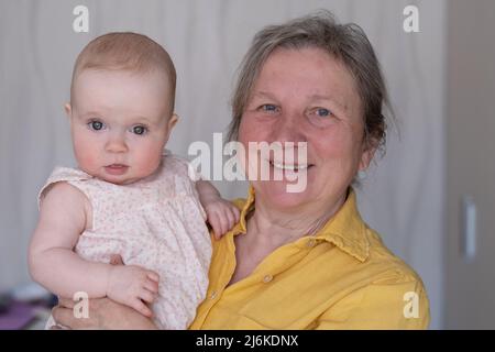 Nonna anziana che tiene un bambino di 7 mesi nelle sue braccia a casa Foto Stock