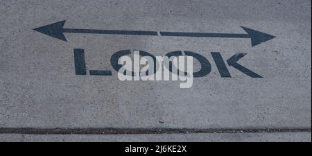 guarda un cartello con frecce che vanno in entrambe le direzioni a sinistra e a destra o ad est e ad ovest dipinte sul marciapiede per cercare i veicoli in arrivo o i treni in direzione opposta Foto Stock