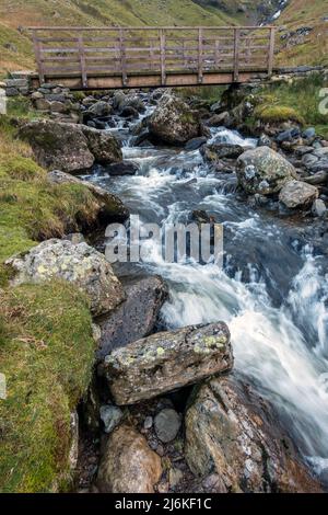 Passerella in legno sul fiume Red Tarn Beck, un ruscello di montagna sotto Helvellyn, Glenridding, English Lake District, Cumbria, UK Foto Stock