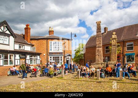 Persone che godono del sole primaverile intorno alle antiche croci sassone nella piazza del mercato della città di mercato Cheshire Sandbach Inghilterra Foto Stock