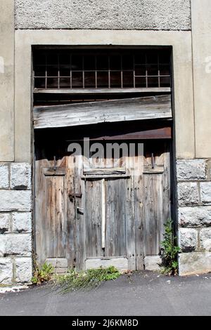 Grandi vecchie porte di ingresso in pannelli di legno fessurati dilapidati per la costruzione industriale abbandonata di fabbrica chiusa con lucchetto arrugginito coperto di legno Foto Stock