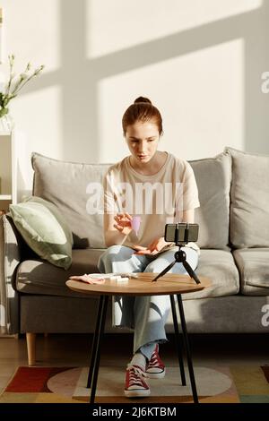 Ritratto minimo di giovane donna caucasica che tiene la tazza mestruale alla macchina fotografica e filma video educativo su prodotti di igiene femminile, spazio copia Foto Stock