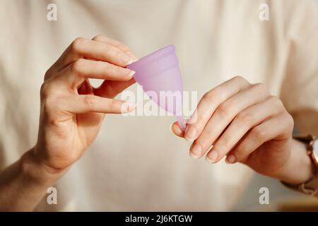 Primo piano minimo della giovane donna che tiene la tazza mestruale rosa e che lo mostra alla macchina fotografica, spazio di copia Foto Stock