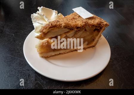 Un pezzo di torta di mele a fette con panna montata sul tavolo nero. Foto Stock