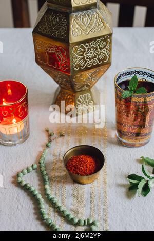 Tavolo con stoffa d'oro, Aleppo peperoncino fiocchi in piatto, candela al crepuscolo, perle di preghiera di giada, tè alla menta Foto Stock