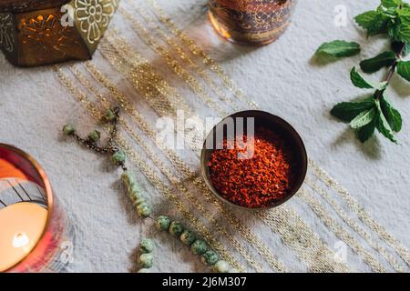 Tavolo con stoffa d'oro, Aleppo peperoncino fiocchi in piatto, candela al crepuscolo, perle di preghiera di giada, tè alla menta Foto Stock