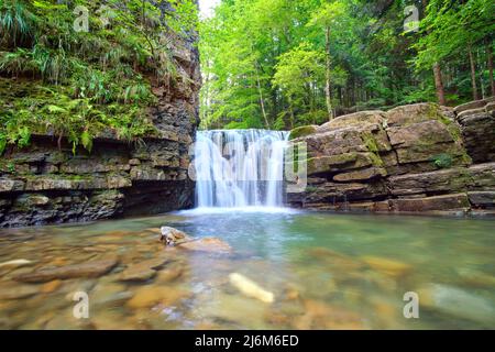 Incredibile paesaggio di splendida cascata sul fiume di montagna con acqua bianca e schiumosa che scende dalla scogliera rocciosa nella foresta pluviale estiva Foto Stock