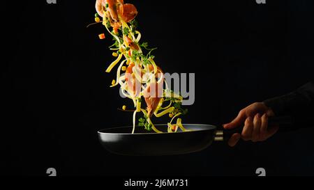 Pasta italiana appetitosa con gamberi e verdure in volo congelato su sfondo nero. Cibo vegetariano sano gourmet, stile di vita sano. R Foto Stock