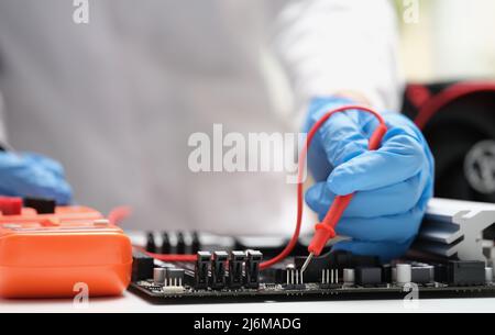 Il tecnico misura la tensione di nella scheda madre del computer utilizzando un multimetro digitale elettronico Foto Stock