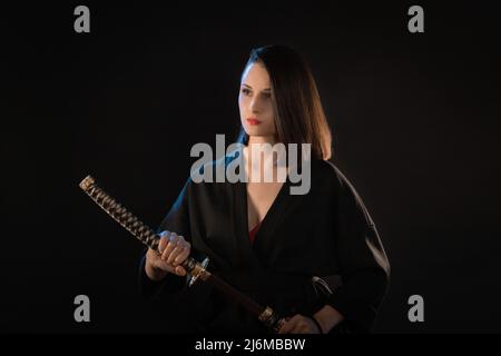 Ritratto di giovane donna bruna kung fu con katana su sfondo nero. Foto Stock
