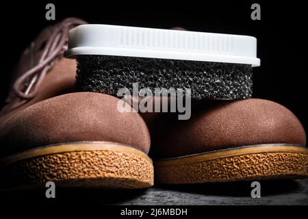 Primo piano di spugna nera in schiuma dura per scarpe scamosciate su stivali marroni. Foto Stock