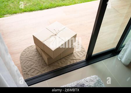 Consegnare la scatola dei pacchi sul tappetino dello sportello vicino alla porta di ingresso Foto Stock