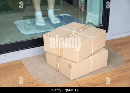 Consegnare la scatola dei pacchi sul tappetino dello sportello vicino alla porta di ingresso Foto Stock