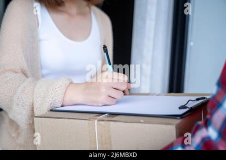 Donna firma i documenti mentre riceve pacchi dal corriere. Concetto di shopping online per consegna e ordine. Foto Stock