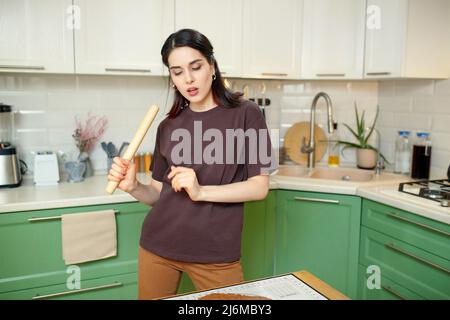 Giovane donna che si aggira intorno, grimacchiando e ballando in cucina. Foto Stock