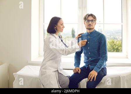 Medico femminile con uno stetoscopio che esamina i polmoni o il cuore di un giovane paziente di sesso maschile Foto Stock