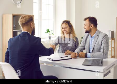 Felice giovane coppia scuotendo le mani con il realtor dopo la firma del contratto al suo ufficio Foto Stock