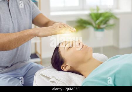 Giovane donna felice, rilassata e calma, con occhi chiusi, che riceve un trattamento reiki sopra la testa. Foto Stock