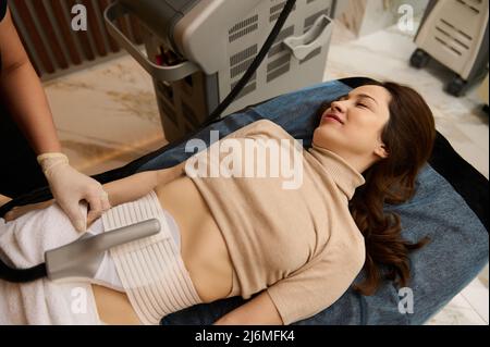 Bella donna in spa medica che riceve un non chirurgico di contornamento del corpo e scultura del corpo utilizzando una moderna apparecchiatura laser lipo di ultima generazione. Anticellulite Foto Stock