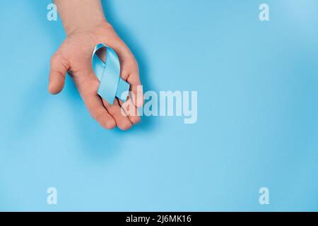 Salute degli uomini e concetto di campagna di sensibilizzazione sul cancro alla prostata. Mano maschio che tiene il nastro blu awareness sul colore sfondo parete in studio con copia spac Foto Stock