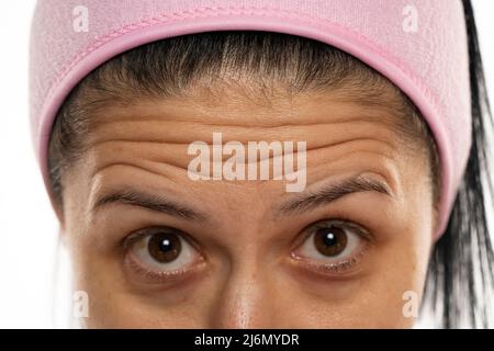 donna di mezza età che mostra le rughe della fronte su uno sfondo bianco Foto Stock