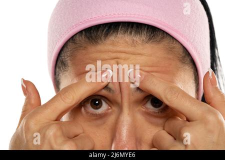 donna di mezza età che mostra la sua fronte rughe con le dita su uno sfondo bianco Foto Stock