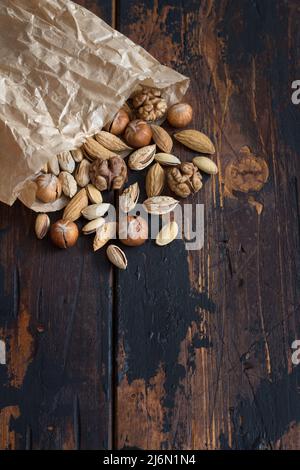 Varietà di noci in pacchetto su tavola di legno. Mandorle, noci, nocciole, pistacchi. Stile rustico, spazio libero, disposizione piatta. orizzontale Foto Stock