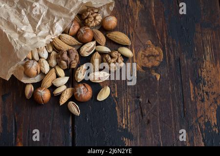 Varietà di noci in pacchetto su tavola di legno. Mandorle, noci, nocciole, pistacchi. Stile rustico, spazio libero, disposizione piatta. orizzontale Foto Stock