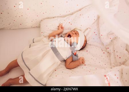 Piangendo e gesturando una bambina di dieci settimane a letto. Foto Stock