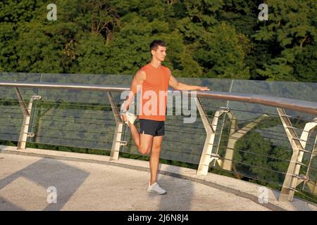 Atletica in abbigliamento sportivo afferra la caviglia con la gamba stretching mano dopo l'allenamento all'aperto, allunga Foto Stock