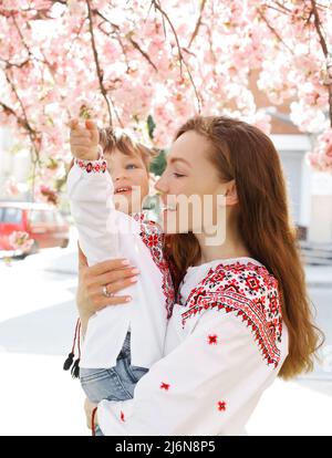 Bambino piccolo sulle mani della madre. Donna che gioca con il bambino fuori nel giardino fiorente della molla. Ritratto della famiglia di due persone. Concetto felice della famiglia. Foto Stock