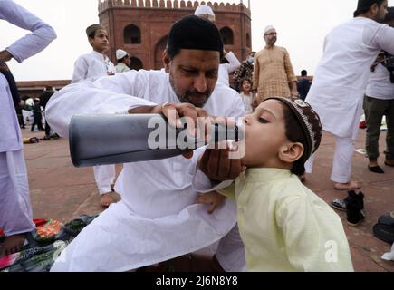 Un padre musulmano ha visto dare acqua al figlio dopo aver offerto preghiere speciali a Eid al-Fitr a Jama Masjid nel quartiere Vecchio. I musulmani di tutto il mondo celebrano Eid al-Fitr, segnando la fine del santo mese di digiuno del Ramadan. Foto Stock