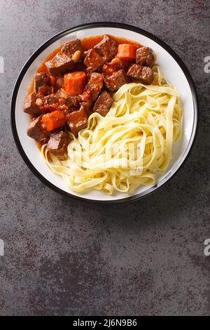 Lo stufato classico francese Daube Provencal viene lentamente cotto a fuoco lento e servito con tagliatelle a spicca nel piatto sul tavolo. Vista dall'alto verticale da Foto Stock