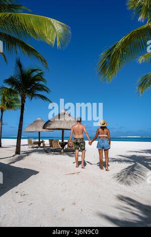 Spiaggia tropicale palme e sabbia bianca blu oceano e lettini spiaggia ombrelloni, sedie a sdraio e ombrelloni sotto una palma su una spiaggia tropicale. Coppia uomini e donne sulla spiaggia tropicale le Morne Mauritius Foto Stock
