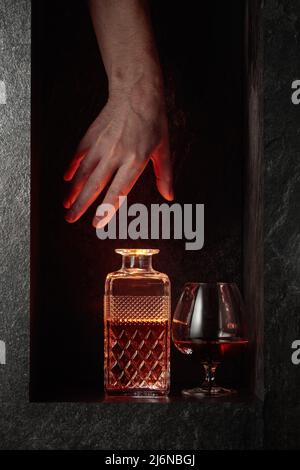 Sbraccio a mano per un decanter di brandy. Un'immagine concettuale sul tema delle bevande costose. Foto Stock