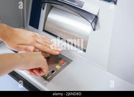 Primo piano delle mani inserimento e occultamento del codice password del numero PIN sulla tastiera della macchina bancaria ATM. Proteggere le operazioni bancarie e le abitudini contro il furto attraverso Foto Stock