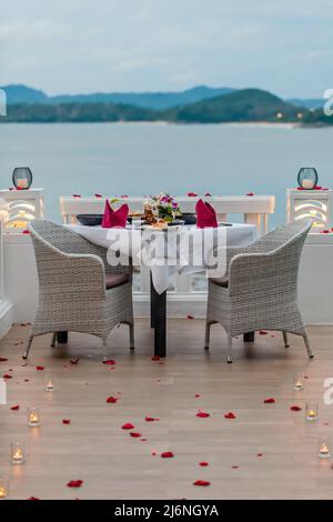 Tavolo per cene romantiche con candele, decorato con petali di rosa nel ristorante Foto Stock