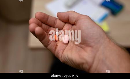 mano dell'uomo che tiene parecchie pillole nella sua mano sullo sfondo domestico di sfocatura. Medicina e concetto di assistenza sanitaria. Foto Stock