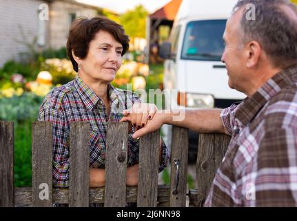 vicini uomo e donna che chiacchierano vicino alla recinzione nel villaggio Foto Stock