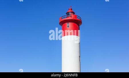 Faro rosso bianco struttura primo piano faro per la sicurezza di avvertimento per navi di mare brutte tempeste tempo contro cielo blu sulla costa. Foto Stock