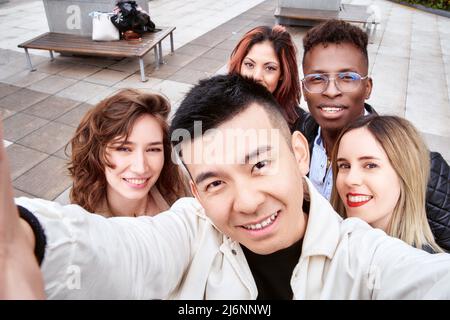 Da sopra l'uomo asiatico sorridendo e prendendo selfie con amici multirazziale il giorno del fine settimana in strada Foto Stock