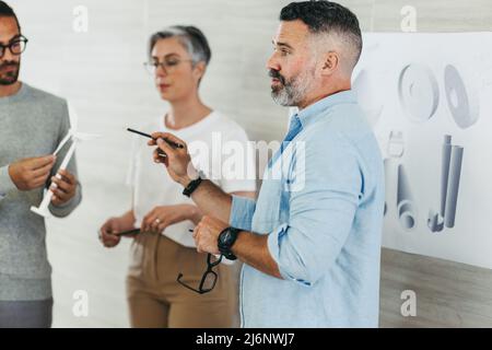 Professionista di design maturo che conduce una discussione durante un incontro con i suoi colleghi. Gli imprenditori creativi condividono idee innovative mentre lavorano o Foto Stock