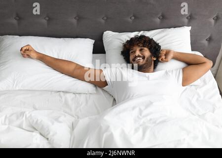 Un ragazzo indiano ben riposato che si allunga nel letto, vista dall'alto Foto Stock