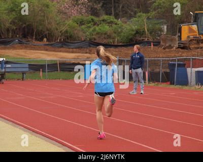 Giovane sprinter femminile che corre il traguardo in un evento di pista della scuola media mentre gli spettatori guardano. Foto Stock