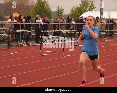 Giovane sprinter femminile che corre il traguardo in un evento di pista della scuola media mentre gli spettatori guardano. Foto Stock